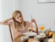 Teen girl in striped shirt at breakfast table with fruits, bread, and juice. Casual morning setting.