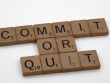 Wooden Scrabble tiles arranged to form the words 'Commit or Quit' on a white background.