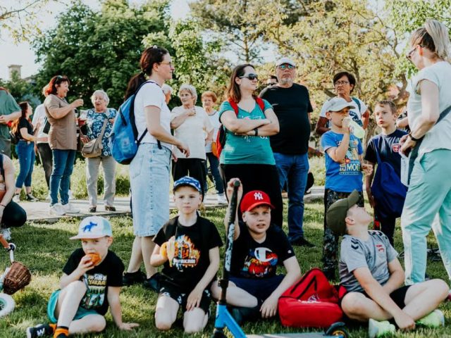 A diverse group of families and children enjoying an outdoor event on a sunny day in a park setting.